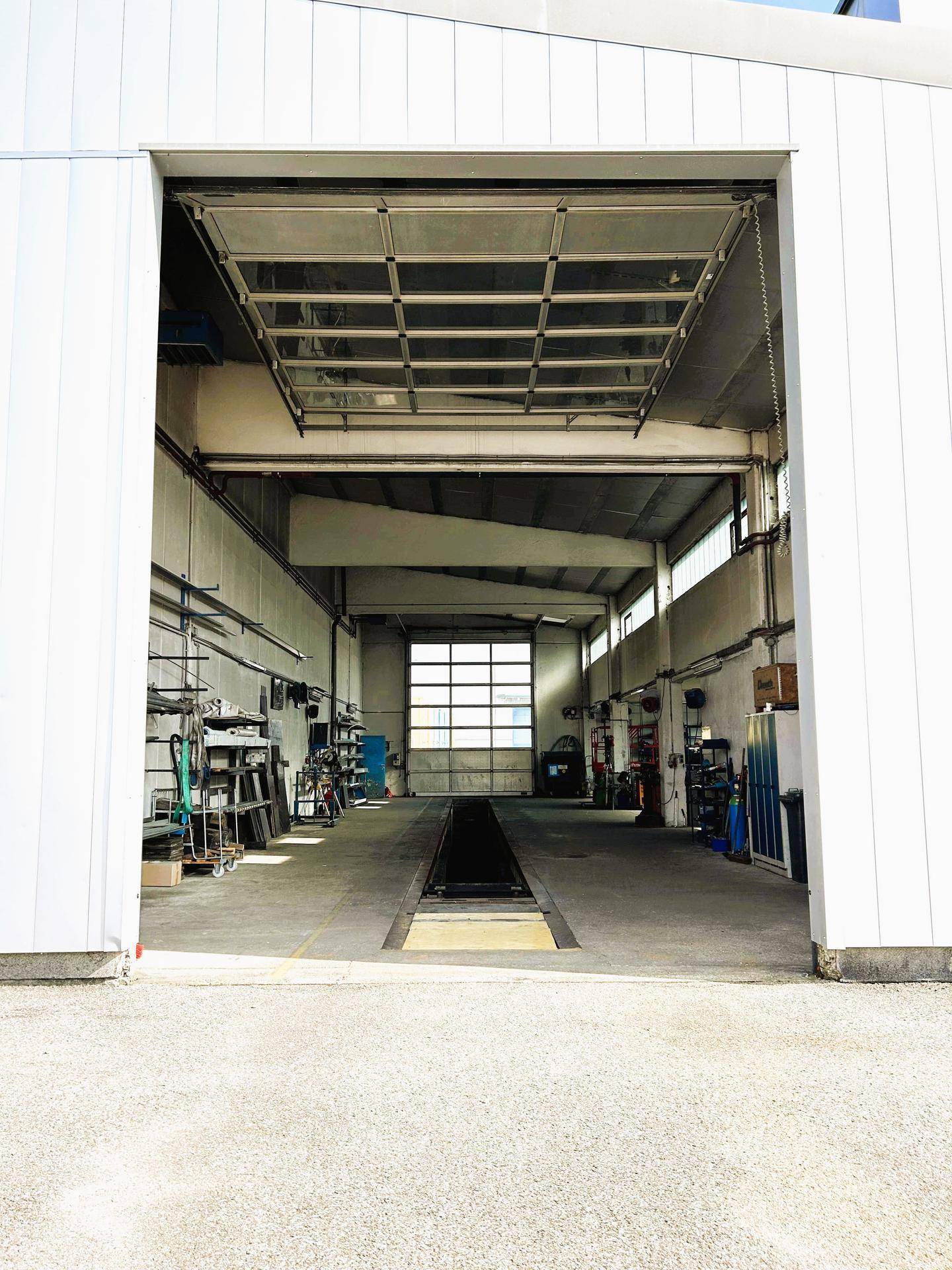 Blick in eine geräumige Werkstatthalle mit offener Rolltoröffnung und einer Inspektionsgrube in der Mitte.