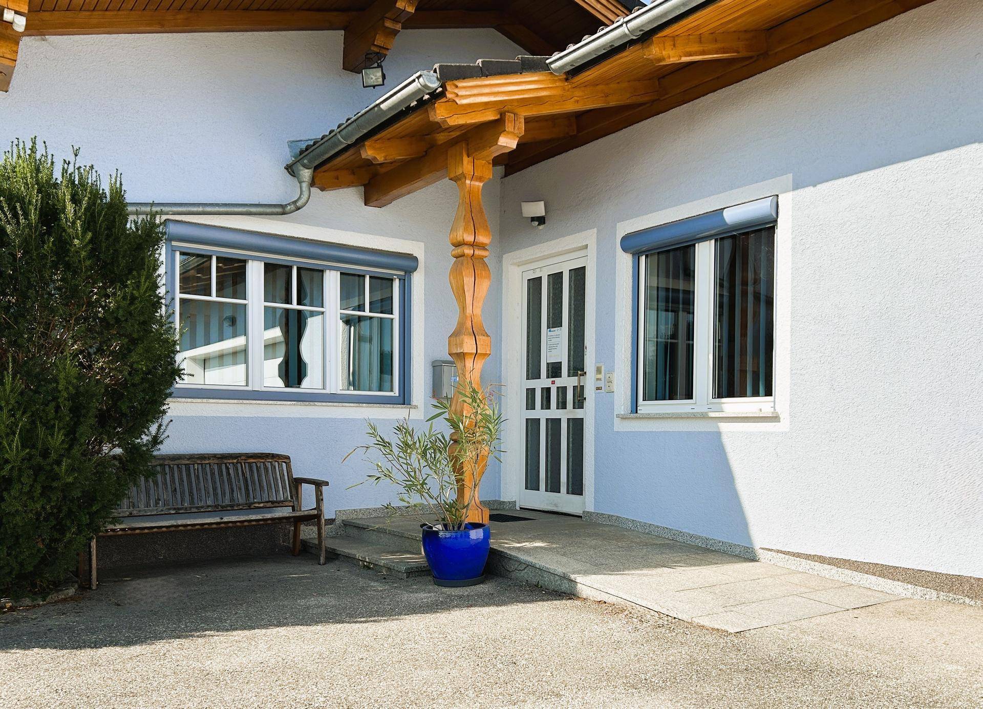 Haupteingang eines Bürogebäudes mit Holzstütze, Rampe und Rollläden an den Fenstern.