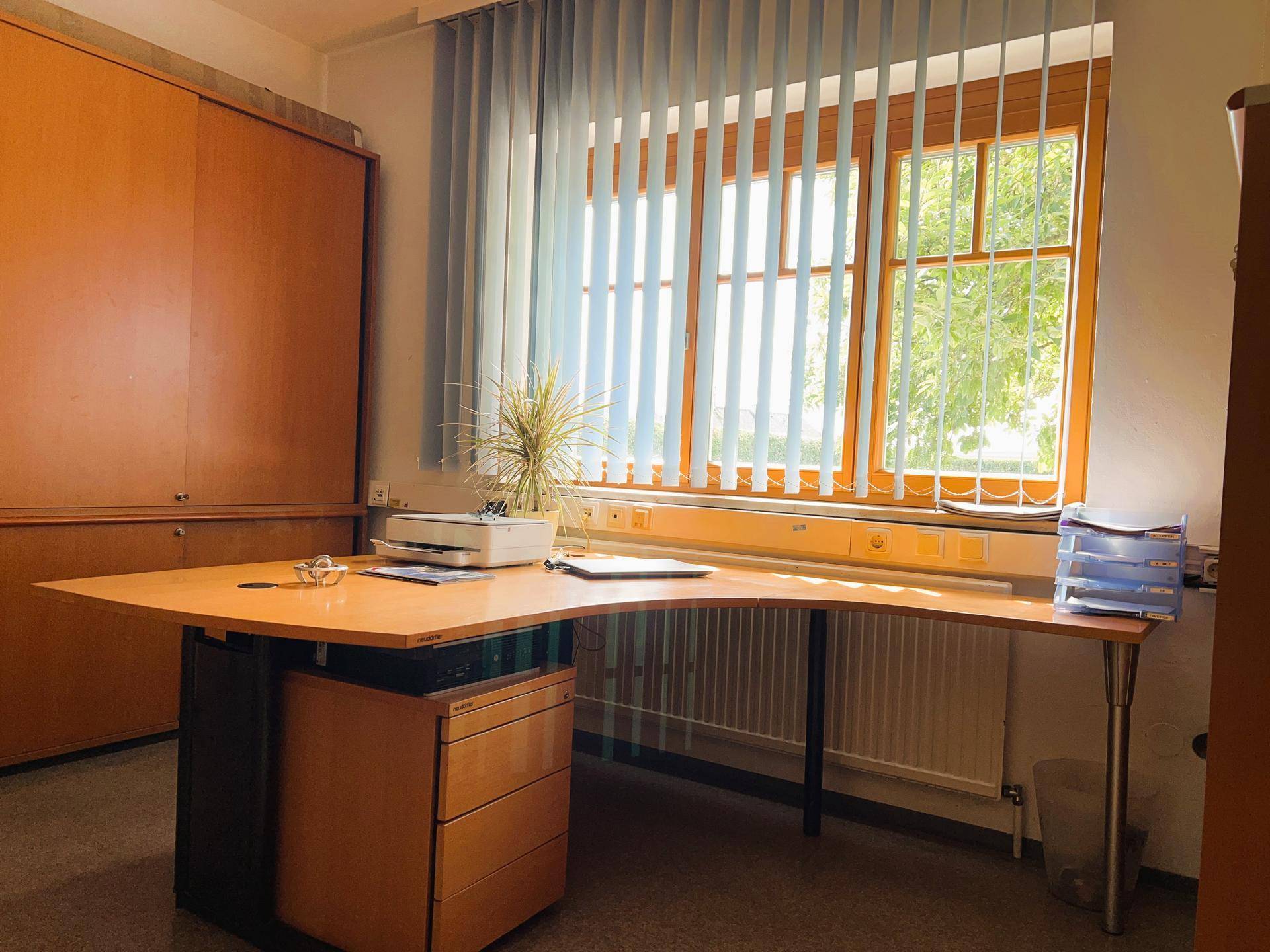 Helles Büro mit großem Fenster und Jalousien, ausgestattet mit einem Schreibtisch und Büromöbeln.