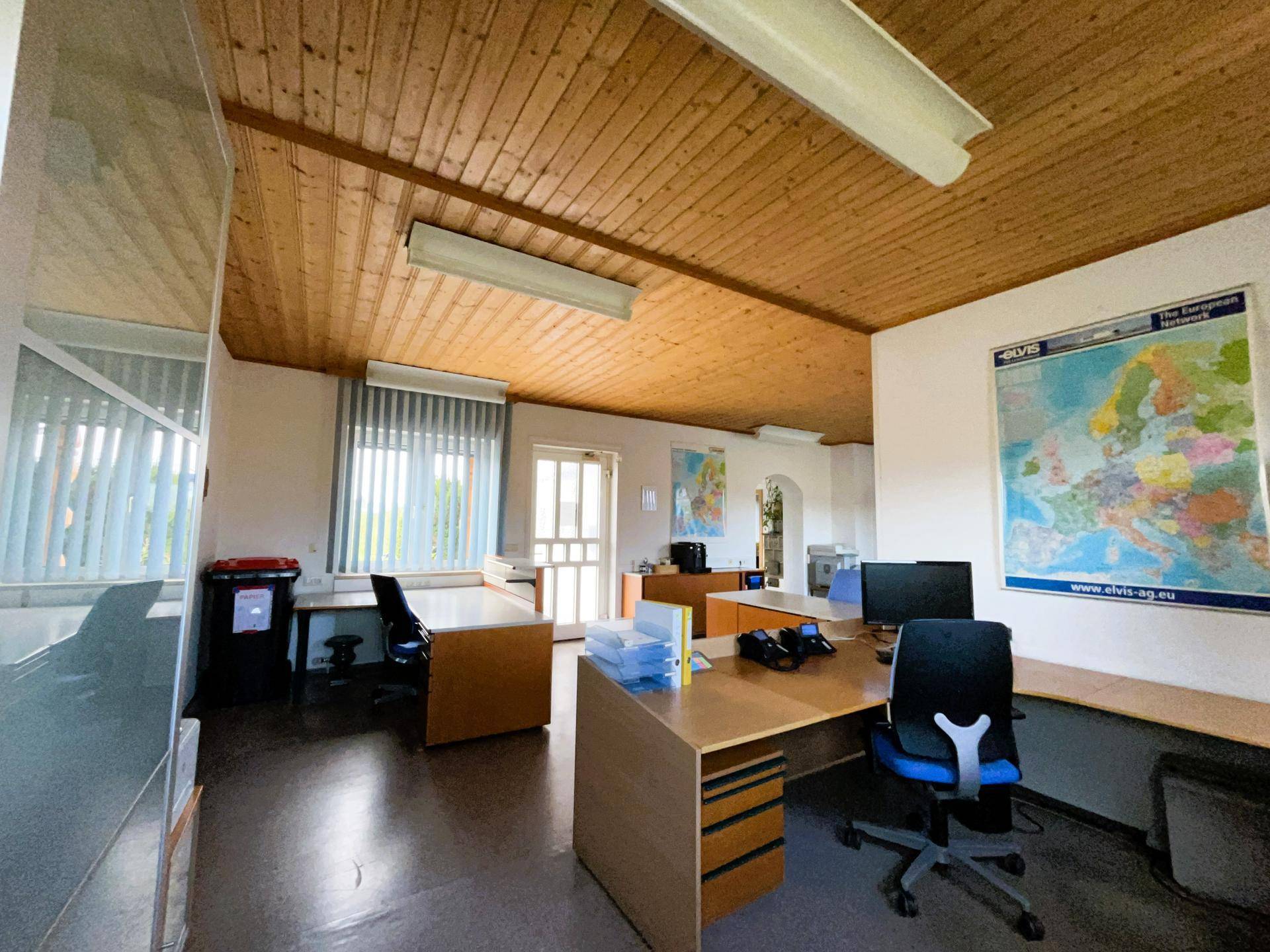 Geräumiges Büro mit Holzdecke, mehreren Schreibtischen und Bürostühlen, gut beleuchtet für den Arbeitsalltag.