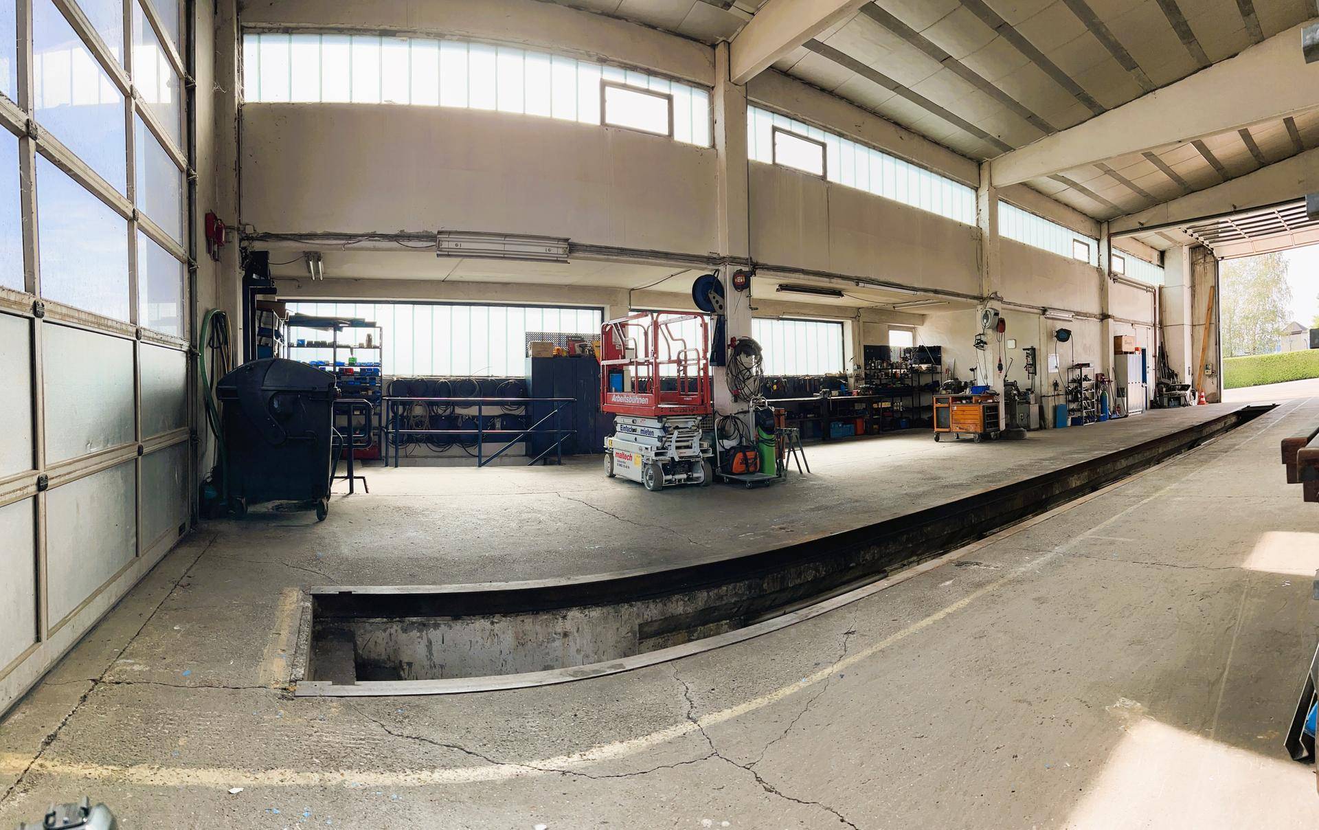 Blick in die Werkstatthalle mit Inspektionsgrube, Werkzeugen und Geräten, die für Reparaturen bereitstehen.
