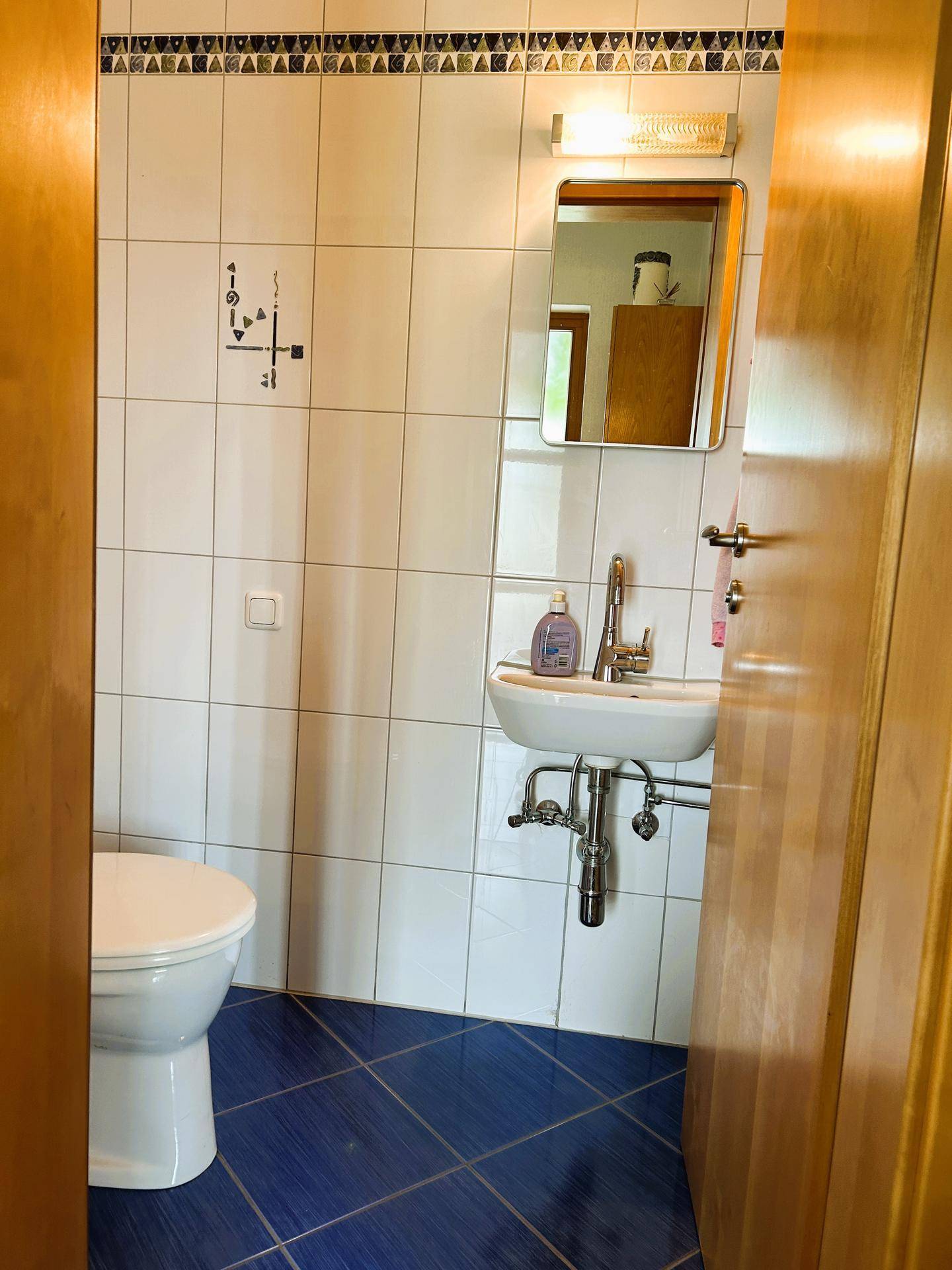 Kleines Badezimmer mit weißen Wandfliesen und blauen Bodenfliesen, ausgestattet mit Toilette und Waschbecken.