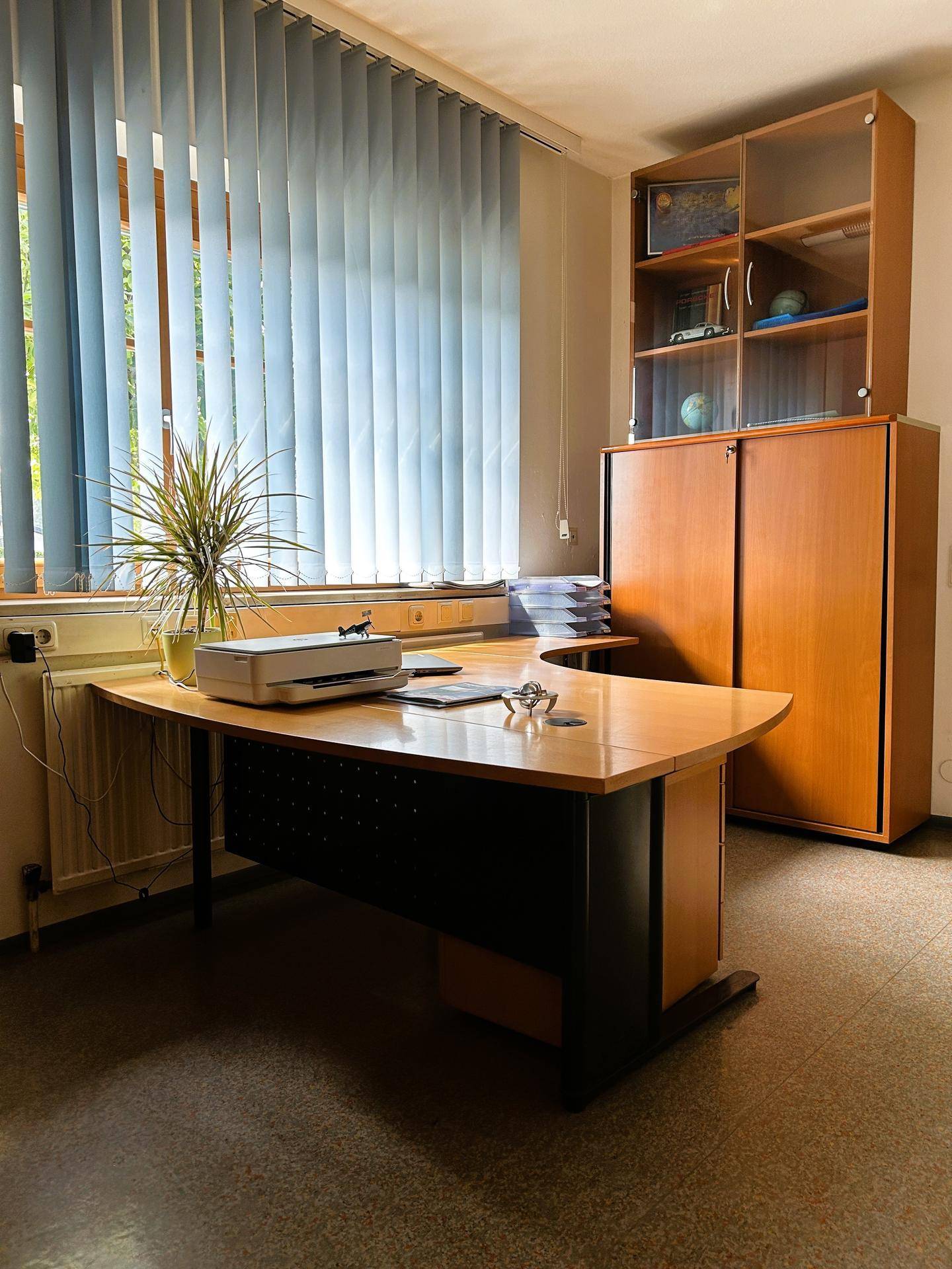 Büro mit großem Schreibtisch und Fenster mit Jalousien, das eine angenehme Arbeitsumgebung bietet.