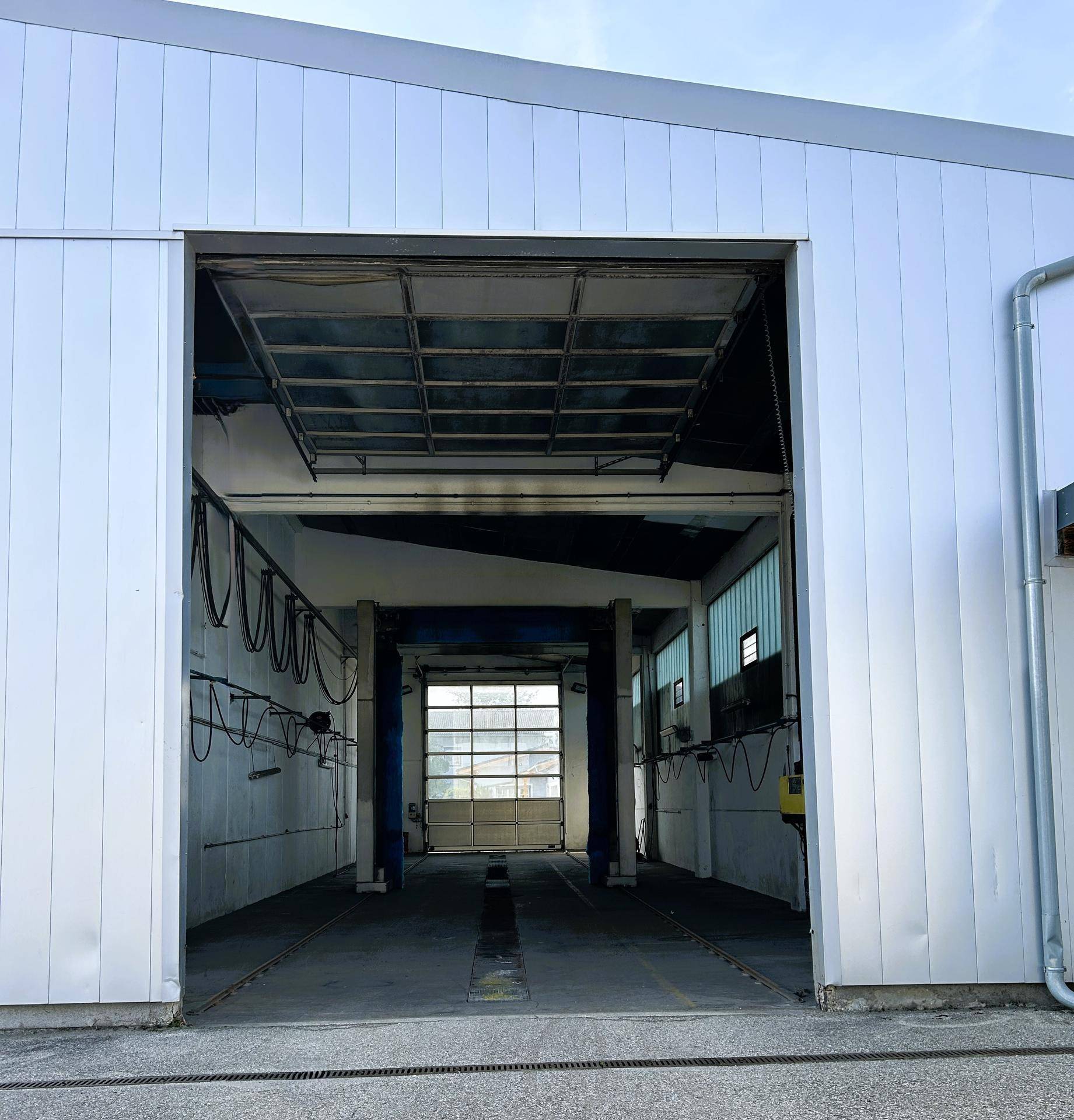 Eingangsbereich der Autowaschanlage mit offenem Rolltor und Blick auf die Waschanlage im Inneren.