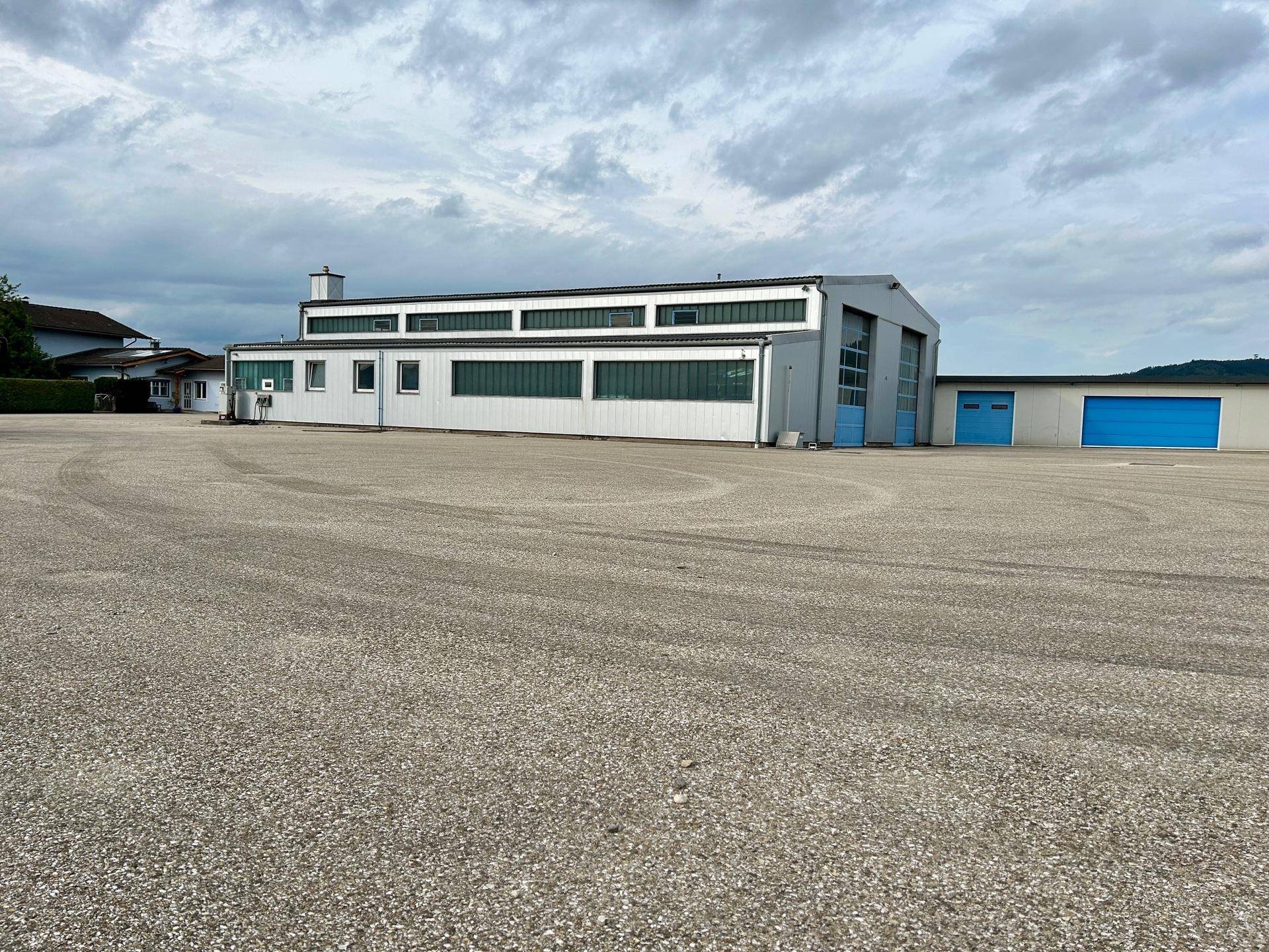 Seitenansicht des Gewerbegebäudes mit langen Fensterbändern und weiteren blauen Toren, umgeben von einem großen Vorplatz.