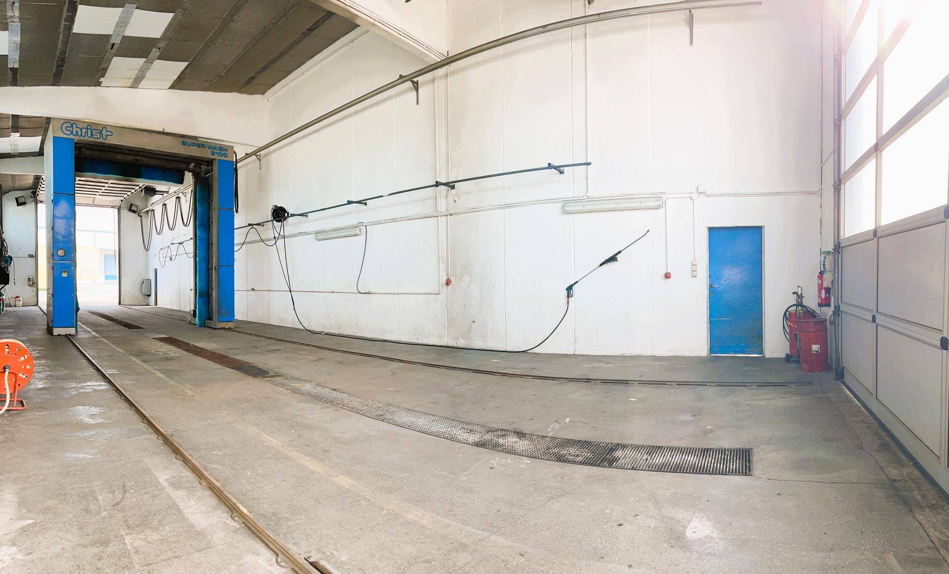 Innenansicht einer Autowaschanlage mit blauer Waschanlage und Entwässerungsrinnen im Boden.