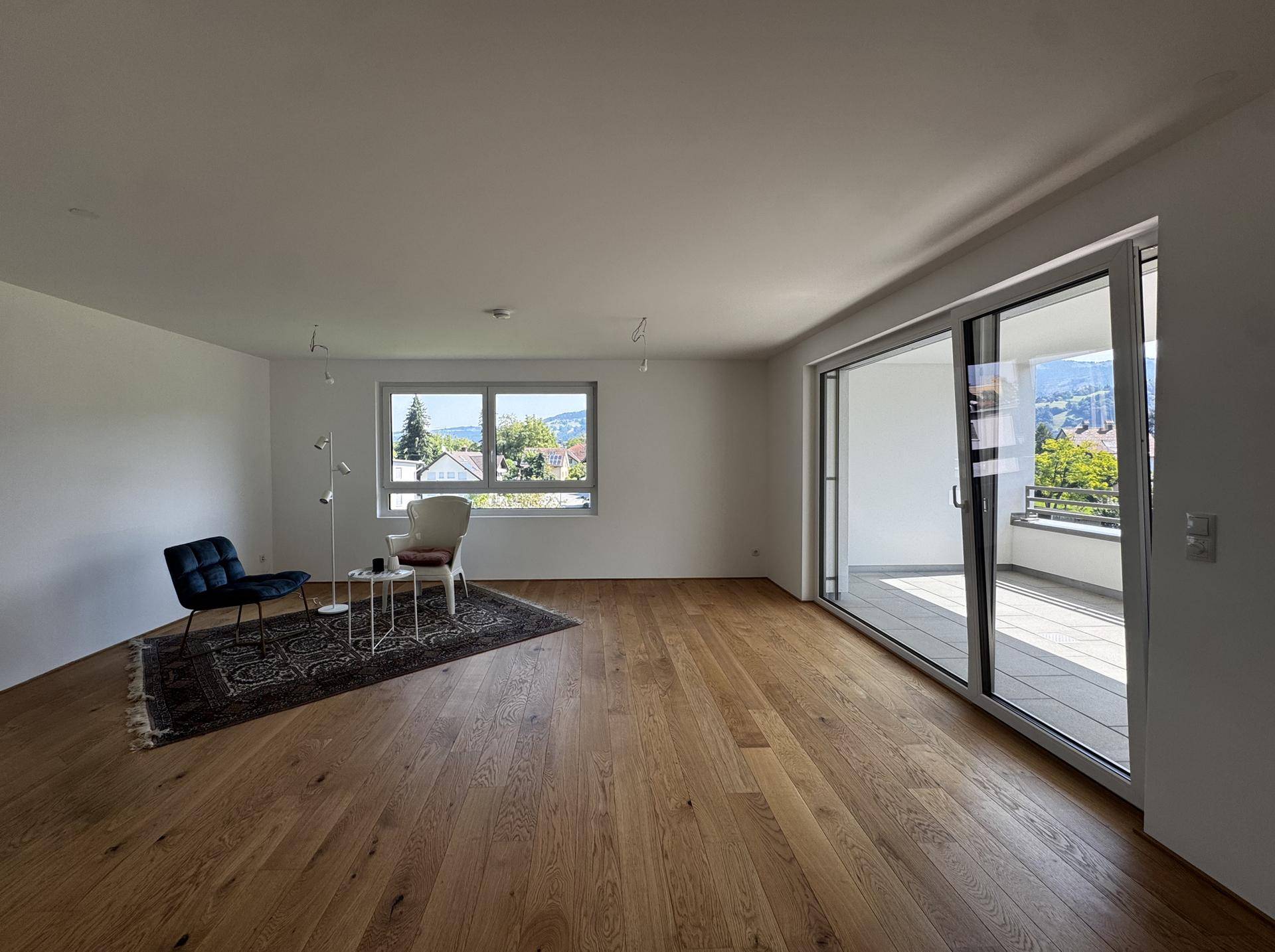Helles Wohnzimmer mit Eichenparkett, großen Schiebetüren zum Balkon und Blick ins Grüne.