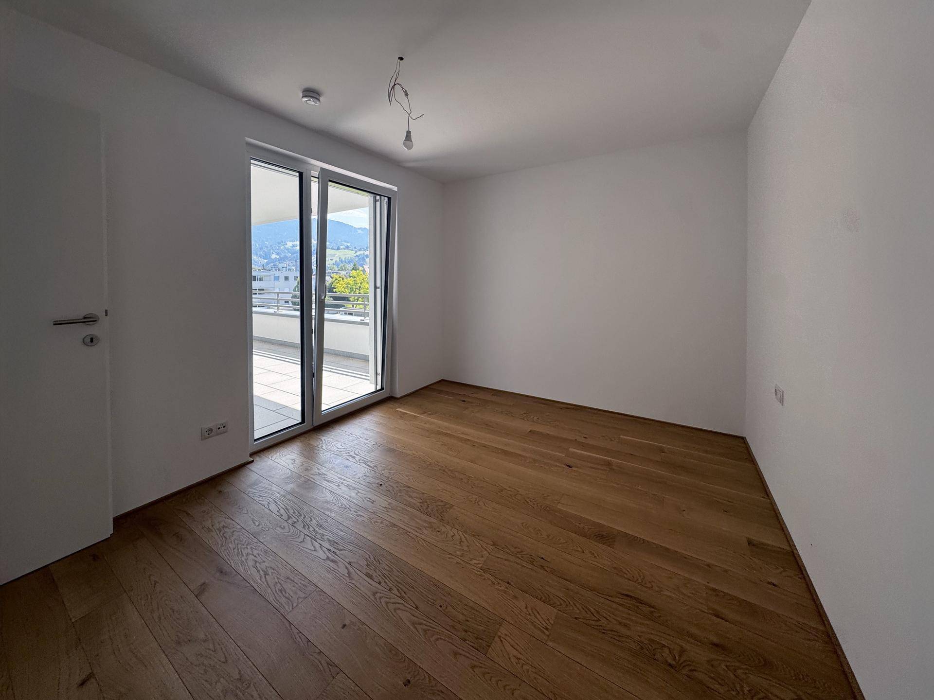 Geräumiges Zimmer mit Holzboden und direktem Zugang zu einem sonnigen Balkon mit Bergblick.
