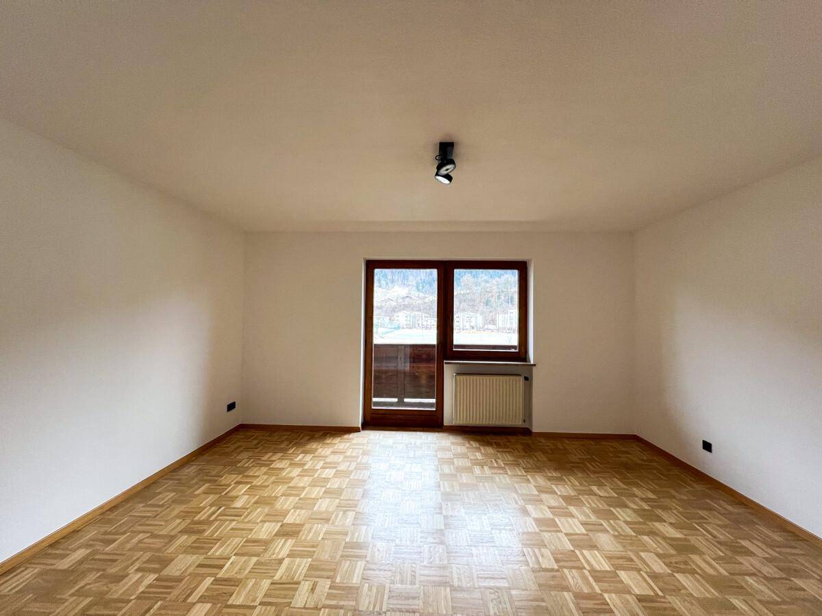 Helles Zimmer mit Parkettboden und Zugang zu einem Balkon oder einer Terrasse.