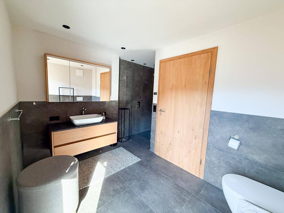 Modernes Badezimmer mit stilvollem Waschbecken, Spiegelschrank und dunklen Fliesen.
