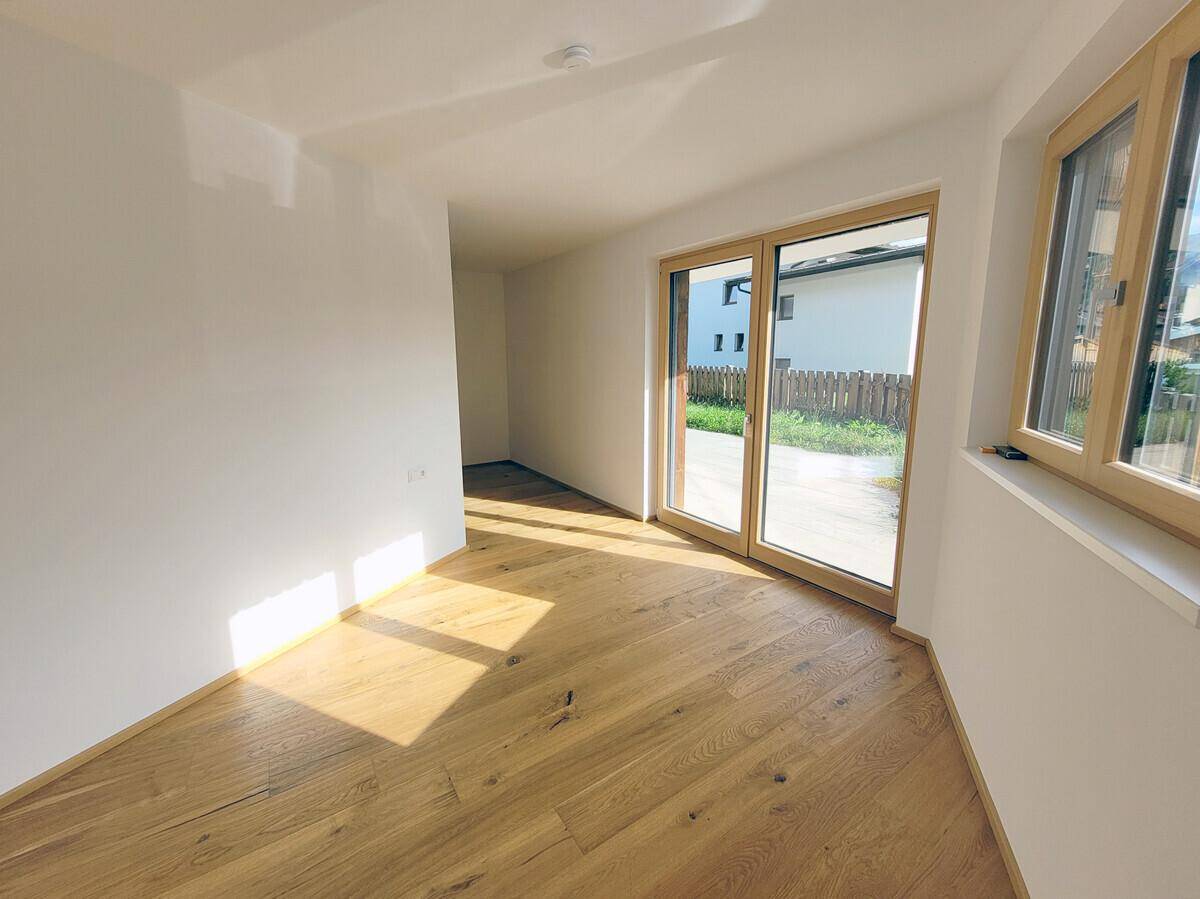 Heller Raum mit Holzboden und großen Fenstern, ideal als Schlaf- oder Arbeitszimmer.