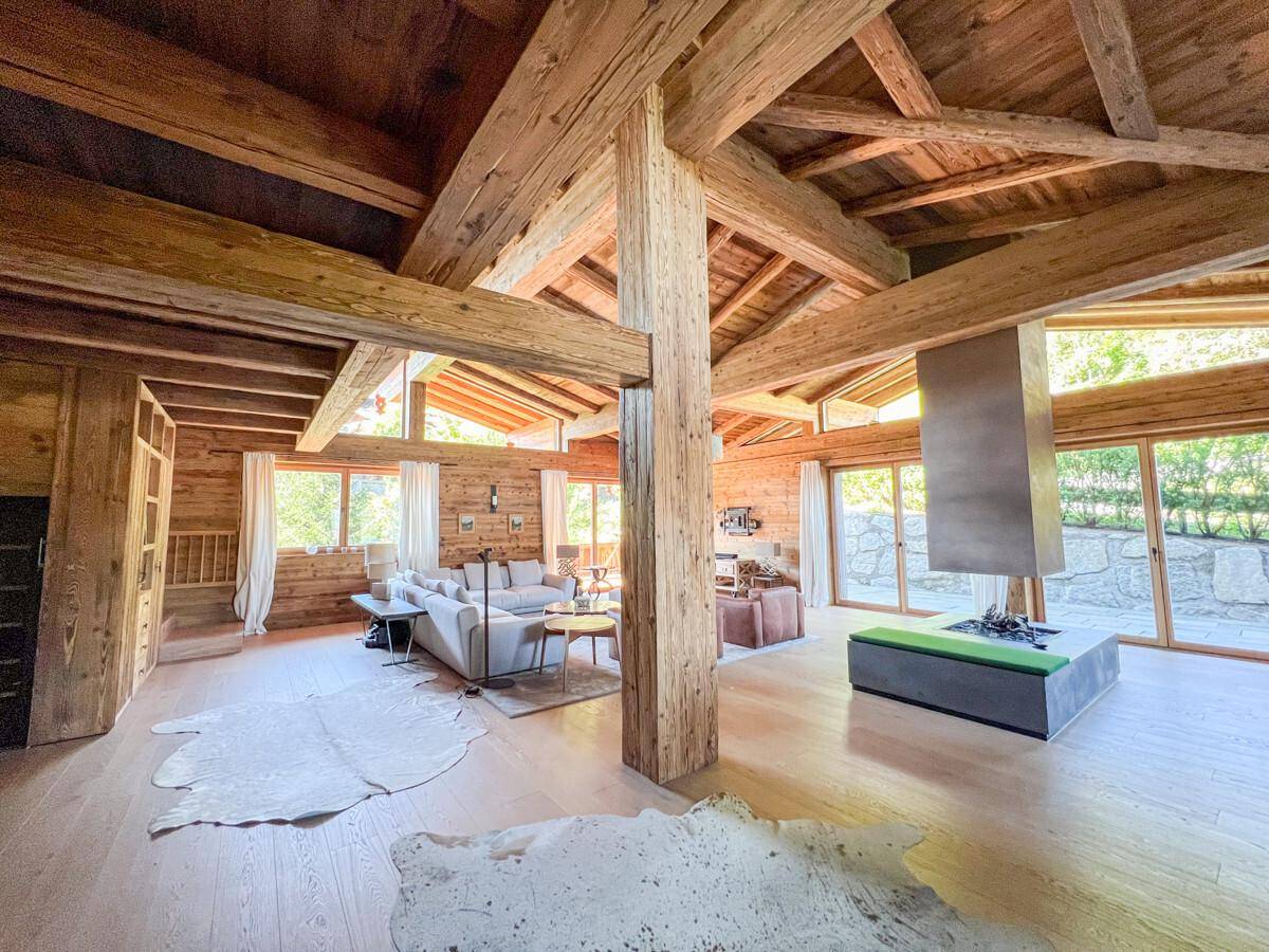 Geräumiger Wohnbereich mit beeindruckenden Holzbalken, modernem Kamin und großen Fensterfronten.