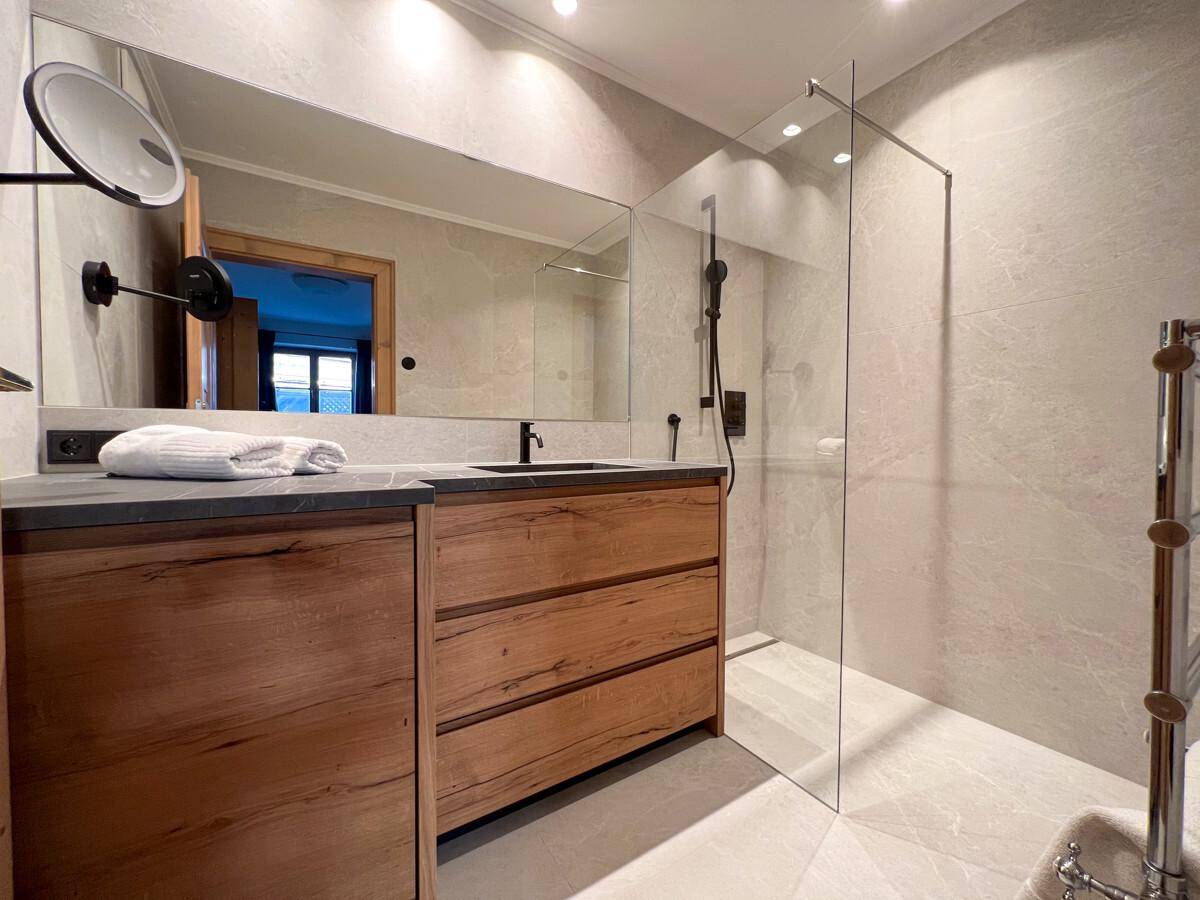 Modernes Badezimmer mit begehbarer Dusche, Holzwaschtisch und großem Spiegel.