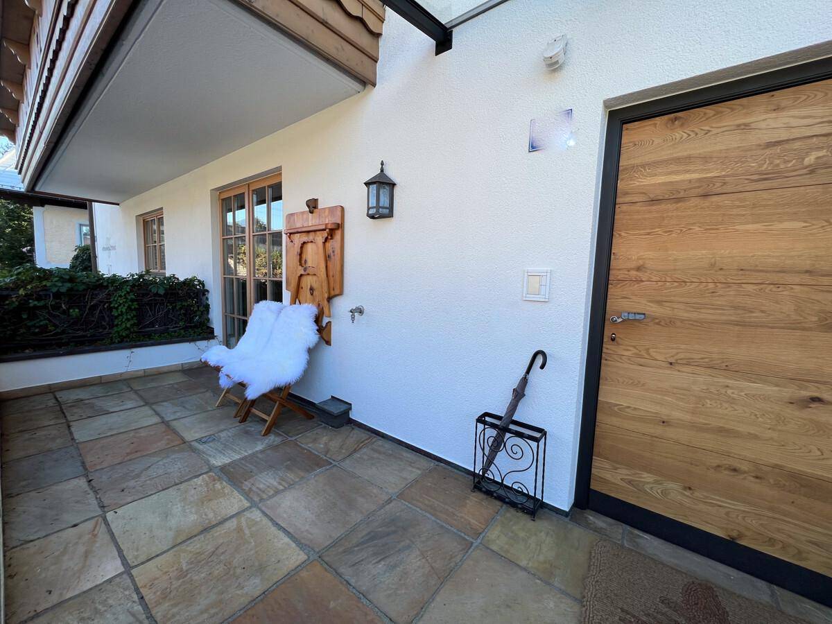 Gemütliche Terrasse mit Steinboden, Holztür und einem Stuhl mit Fellauflage.