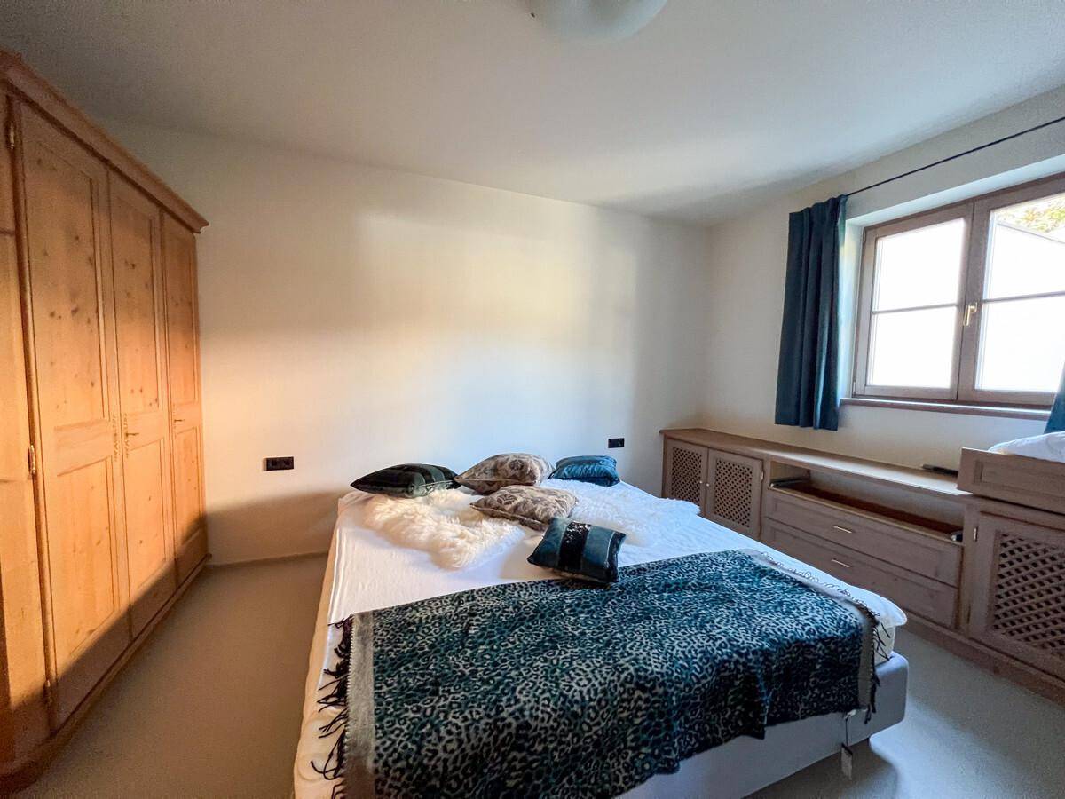 Schlafzimmer mit großem Holzkleiderschrank, Doppelbett und Fenster mit Tageslicht.