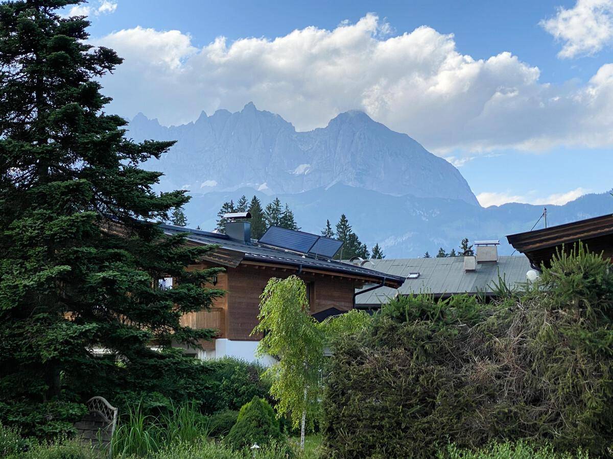 Häuser mit Holzfassaden und Solaranlagen auf den Dächern vor einer beeindruckenden Bergkulisse.