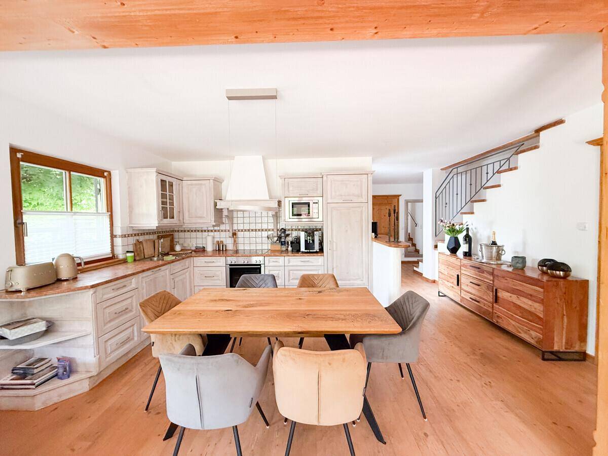 Helle Einbauküche mit Essbereich, Holztisch und Blick auf die Treppe.