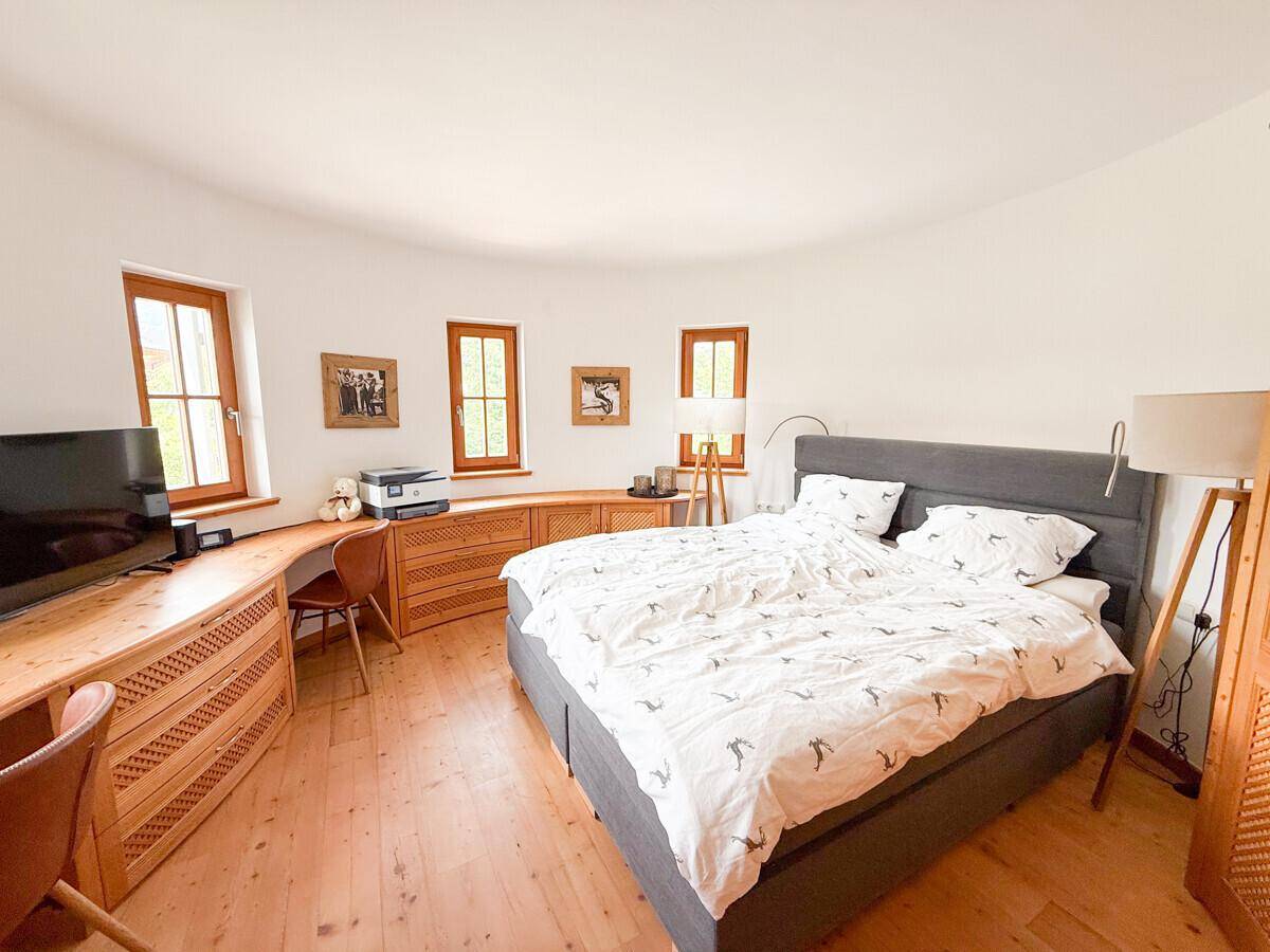 Geräumiges Schlafzimmer mit Doppelbett, Holzmöbeln und mehreren Fenstern für viel Licht.