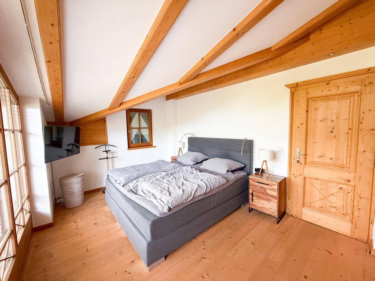 Helles Schlafzimmer mit großem Bett, Holzboden und sichtbaren Holzbalken an der Decke.