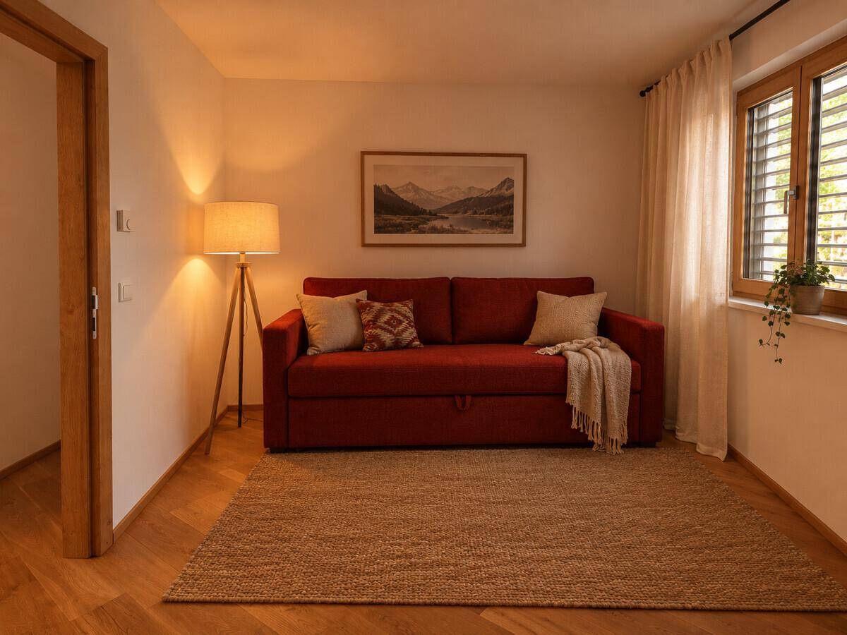 Gemütliches Zimmer mit rotem Schlafsofa, Stehlampe und Fenster mit Blick ins Grüne.