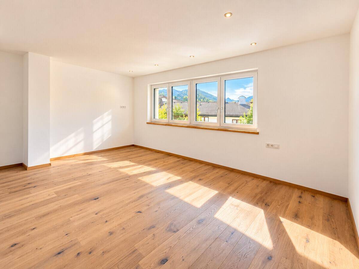 Heller, leerer Raum mit Holzboden und großen Fenstern, die viel Tageslicht hereinlassen.