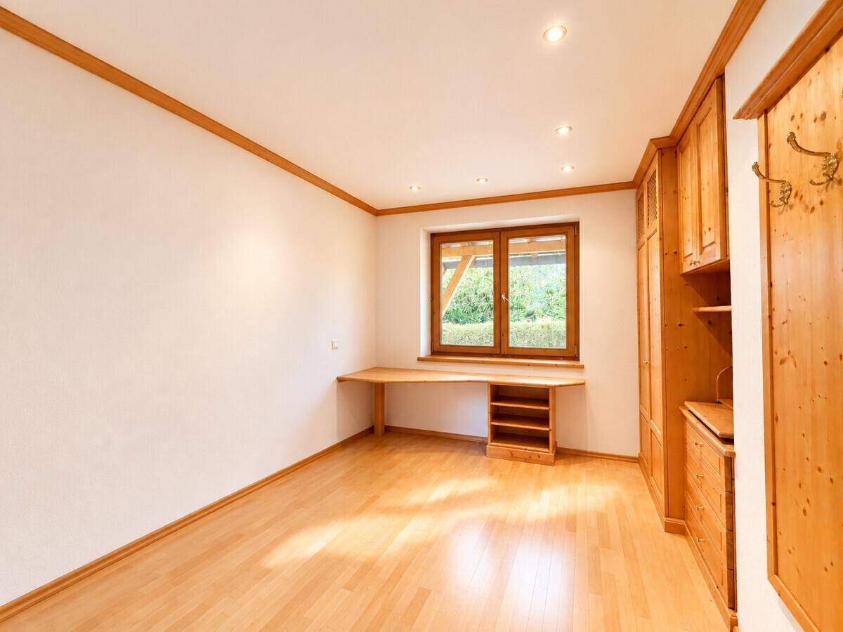 Helles Arbeitszimmer mit Holzboden, Einbauschränken und einem großen Schreibtisch am Fenster.