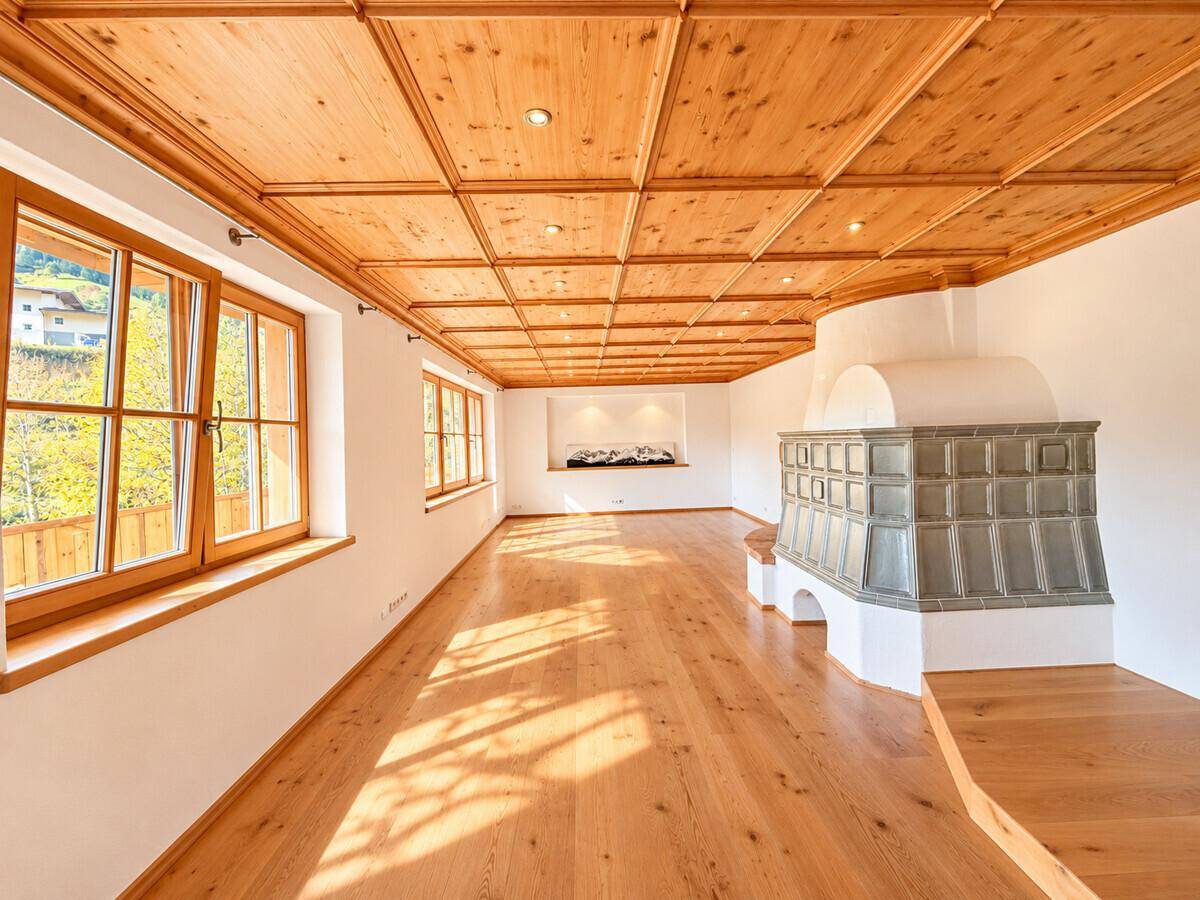 Geräumiges Wohnzimmer mit traditionellem Kachelofen, Holzbalkendecke und Holzboden, hell und einladend.