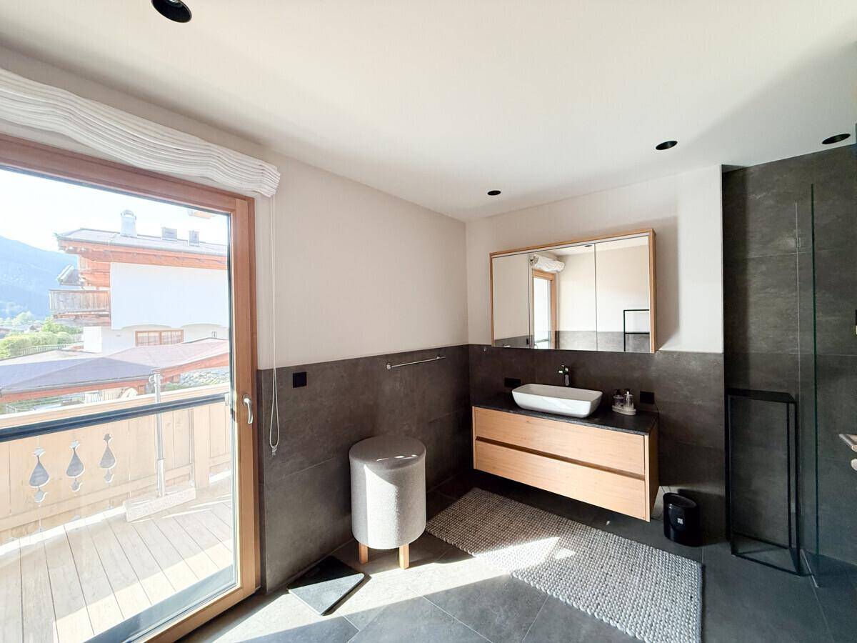 Helles Badezimmer mit modernem Design, Fenster und Zugang zu einem Außenbereich.