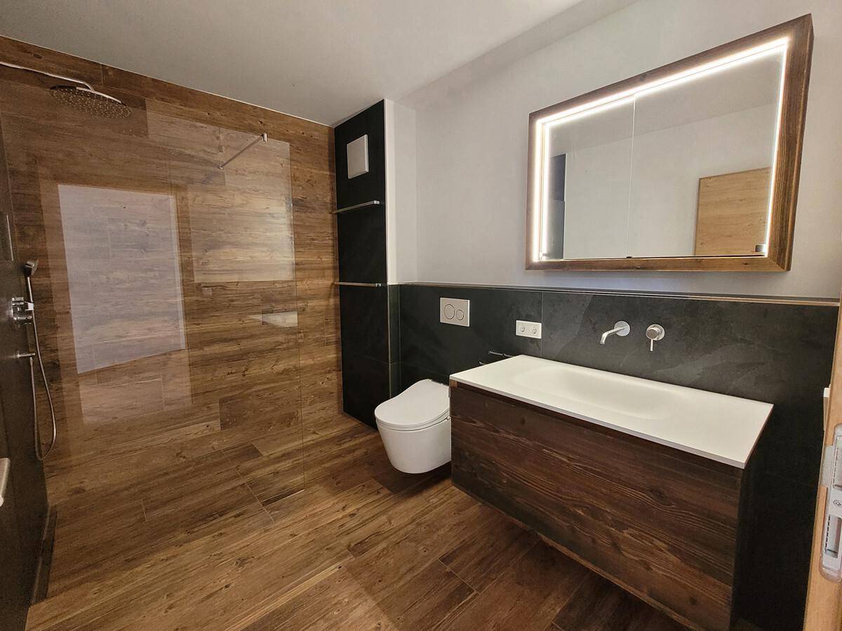 Modernes Badezimmer mit begehbarer Dusche, Holzoptik-Fliesen und beleuchtetem Spiegelschrank.