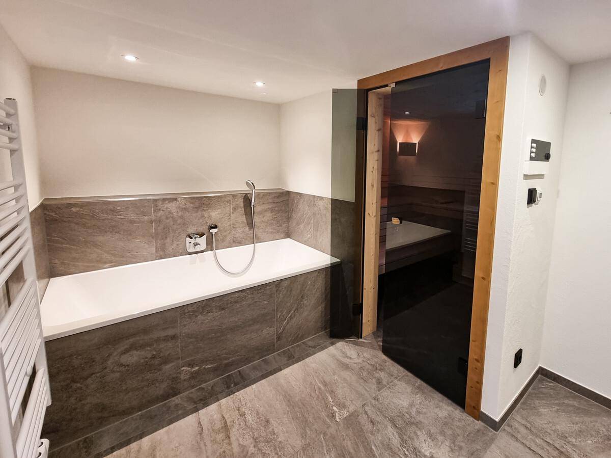 Geräumiges Badezimmer mit Badewanne, Fliesenboden und integrierter Sauna für Wellnessmomente.