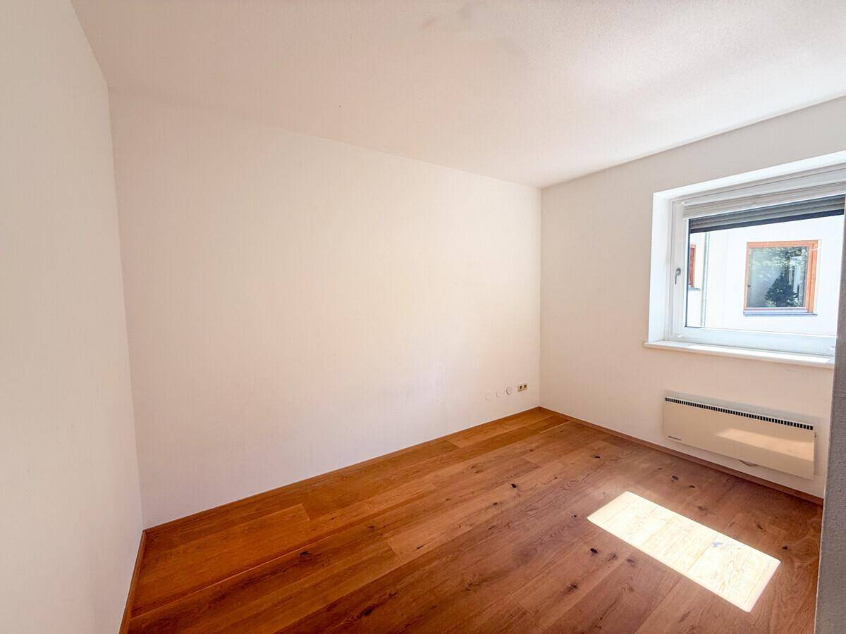 Einfaches Schlafzimmer mit Holzboden und einem Fenster mit Rollladen, sauber und hell.