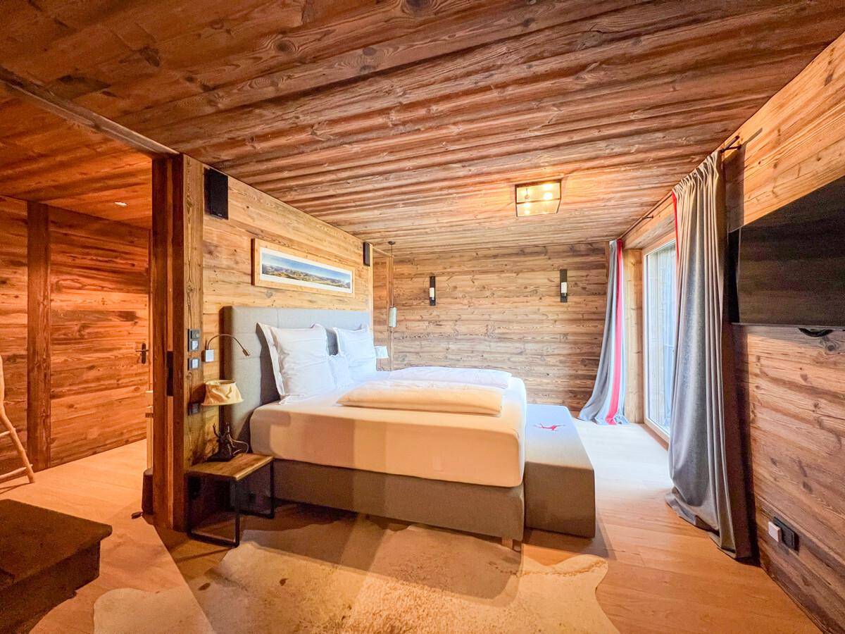 Gemütliches Schlafzimmer mit Holzwänden, großem Bett und Zugang zu einem Balkon oder Garten.