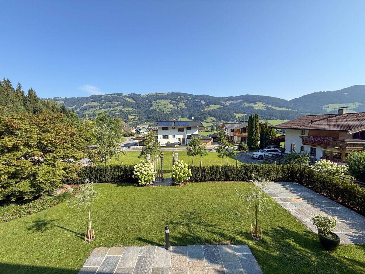 Gepflegter Garten mit Rasenfläche, Steinplattenweg und weitem Blick auf die umliegende Berglandschaft.