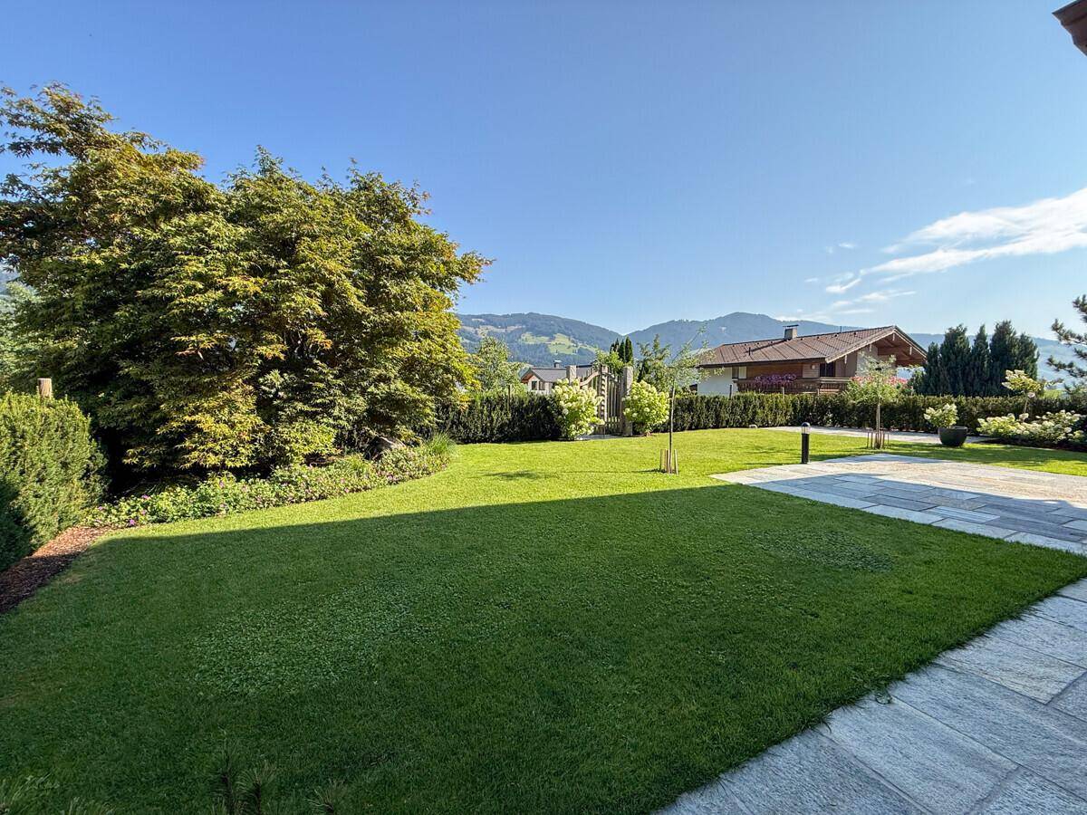 Weitläufiger Garten mit gepflegtem Rasen, Steinplatten und Panoramablick auf die Bergwelt.