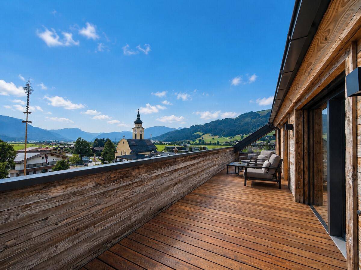 Geräumige Holzterrasse mit Sitzgruppe und Blick auf das Dorf und die Berge.