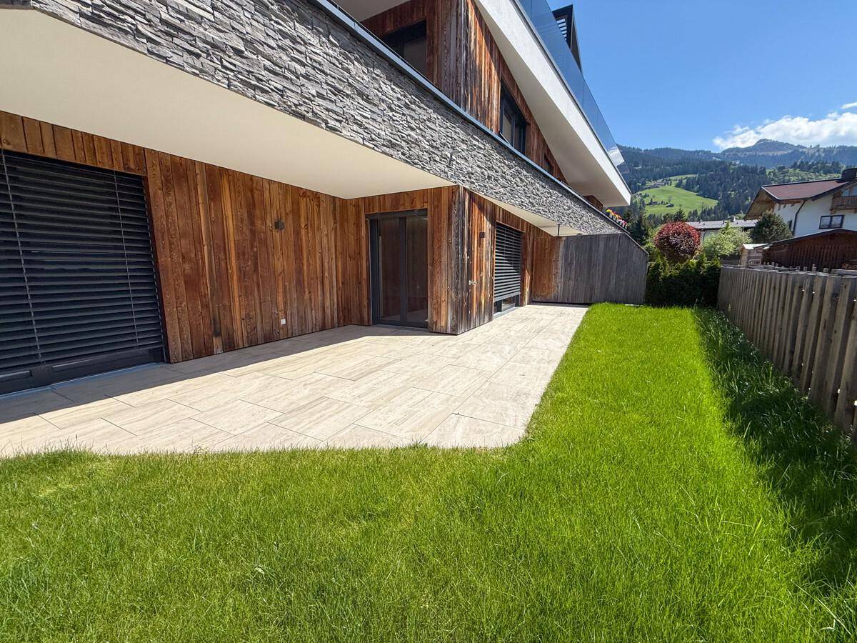 Geräumige Terrasse mit Fliesenboden und angrenzendem Rasenbereich vor der modernen Fassade.