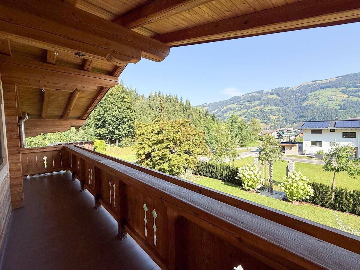 Traditioneller Holzbalkon mit geschnitztem Geländer und Panoramablick auf die grüne Umgebung und Berge.