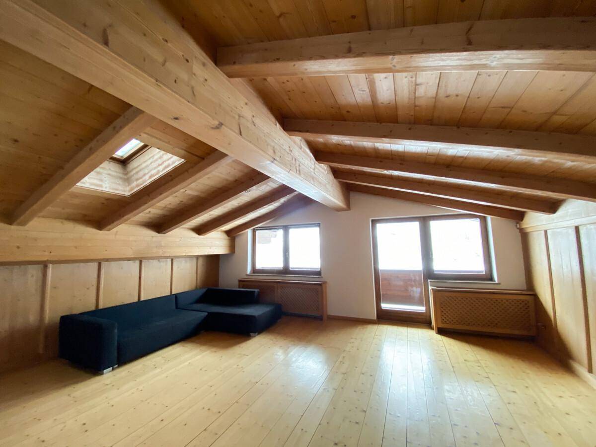 Heller Wohnbereich mit Holzbalkendecke, Dachfenster und Zugang zu einem französischen Balkon.