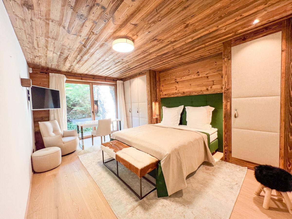 Helles Schlafzimmer mit Holzwänden, grünem Bett, Einbauschränken und Schreibtischbereich.