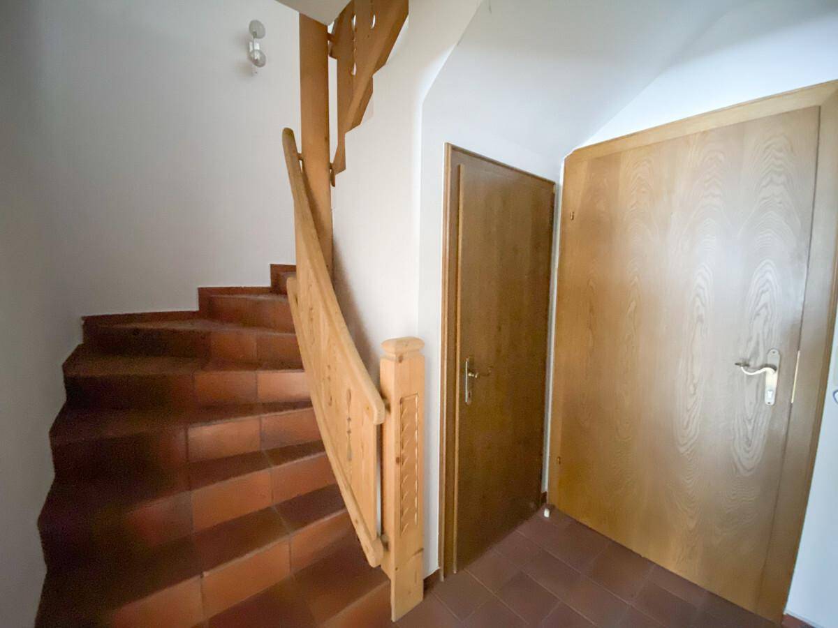 Treppenhaus mit Holzgeländer und Terrakottafliesen, das verschiedene Ebenen verbindet.