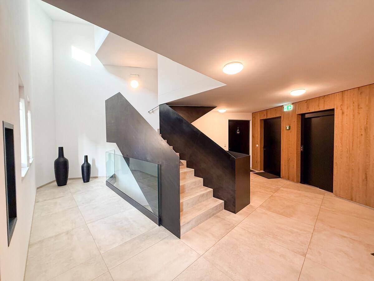 Modernes Treppenhaus mit eleganten Stufen, Glasgeländer und Zugang zu den Wohneinheiten.