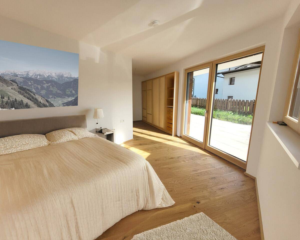 Helles Schlafzimmer mit Holzboden, großem Bett und Zugang zu einem Außenbereich.