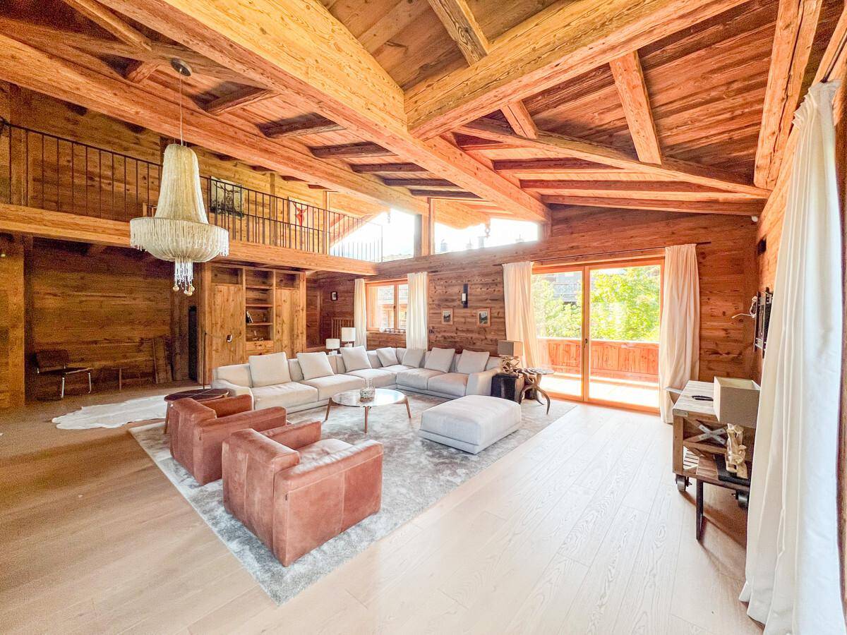 Gemütlicher Wohnbereich mit Holzbalken, bequemen Sofas, Kronleuchter und Zugang zu einem Balkon.