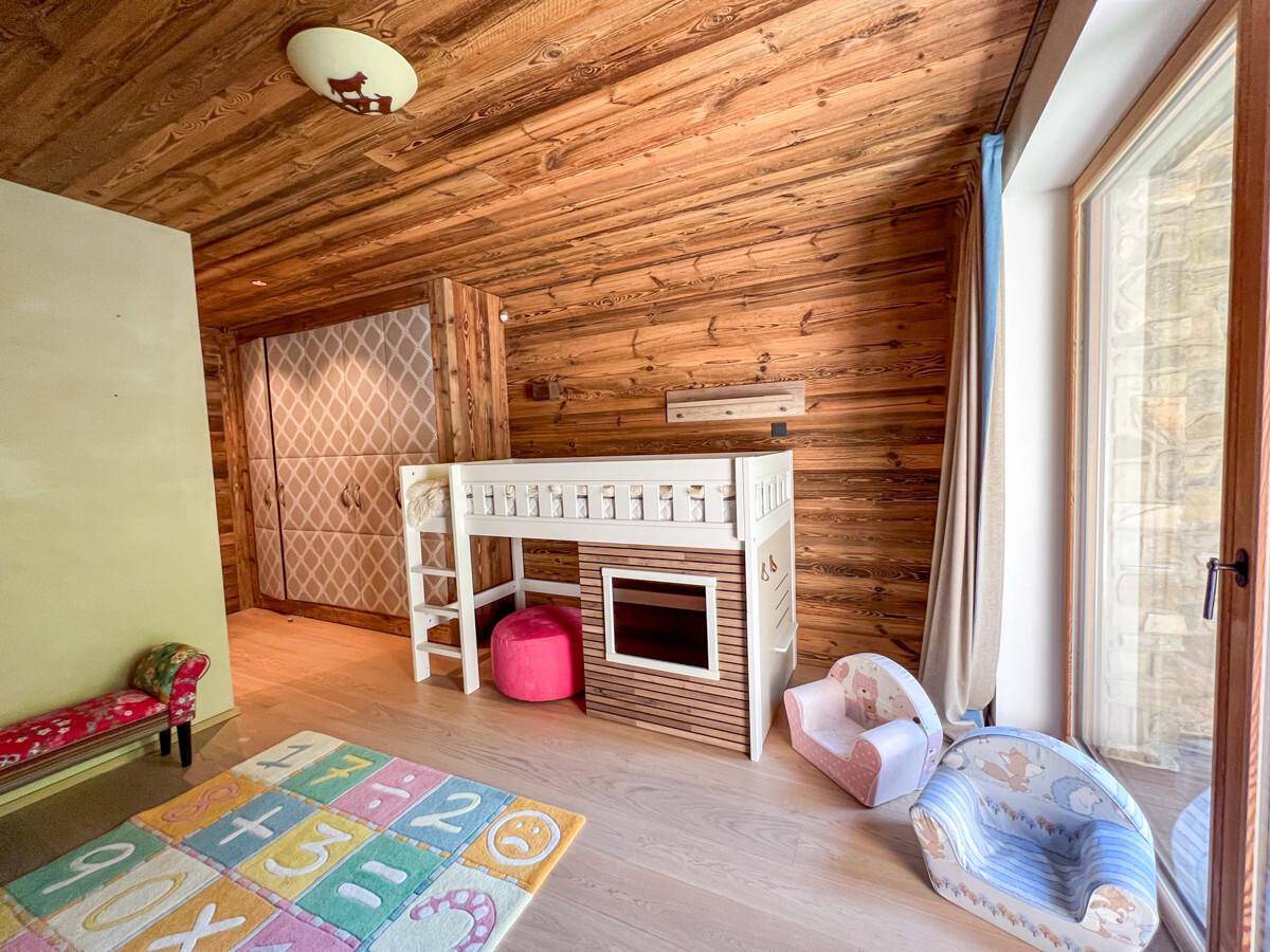 Helles Kinderzimmer mit Hochbett, Spielteppich und großen Fenstern.