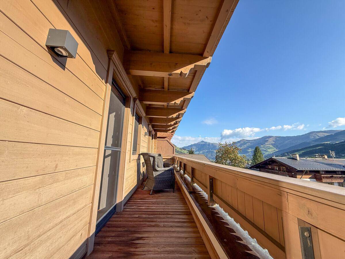 Langer Holzbalkon mit Sitzgelegenheit und malerischem Blick auf die umliegenden Berge.