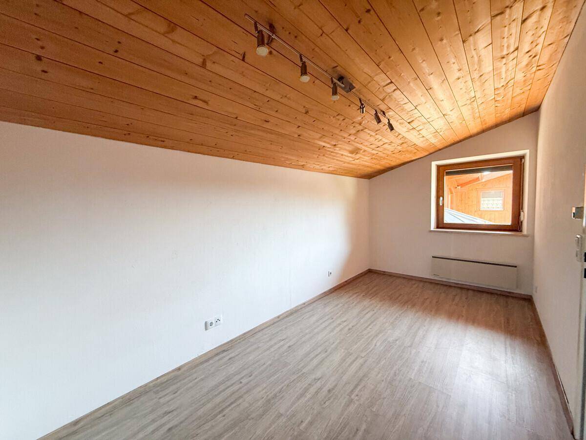 Helles Dachzimmer mit Holzbalkendecke, Laminatboden und schrägem Fenster, sehr einladend.
