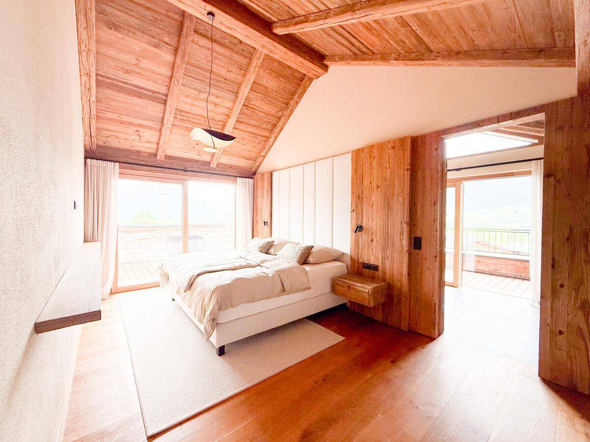 Helles Schlafzimmer mit Holzbalkendecke, Doppelbett und Zugang zu einem Balkon.
