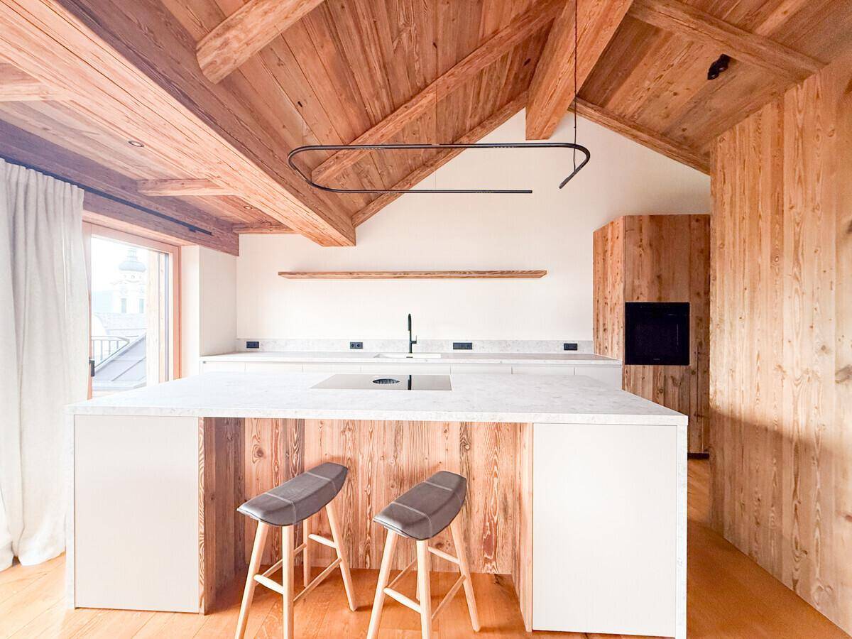Moderne Küche mit Kochinsel, integrierten Geräten und Holzwänden unter einer Holzbalkendecke.