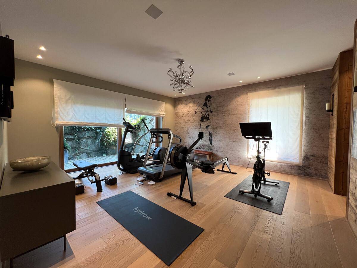 Gut ausgestatteter Fitnessraum mit verschiedenen Trainingsgeräten und großen Fenstern.
