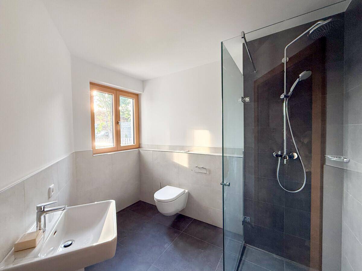 Helles Badezimmer mit Dusche, Fenster und modernen Armaturen in neutralen Farbtönen.